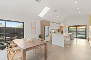A modern kitchen with a central island, a dining area with a wooden table and chairs, and large windows providing natural light.