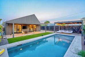 Ein modernes Haus mit Swimmingpool, Sitzgelegenheiten im Freien und einer überdachten Terrasse.