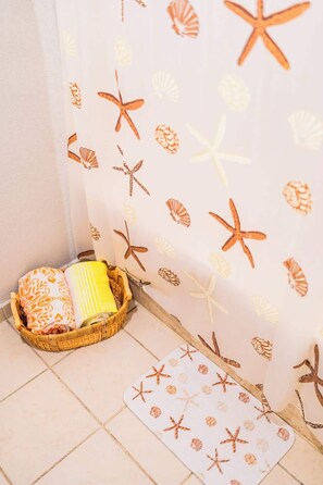 Un rincón de una habitación con suelo de baldosas, una cesta de mimbre con almohadas y una pared decorada con motivos marinos.
