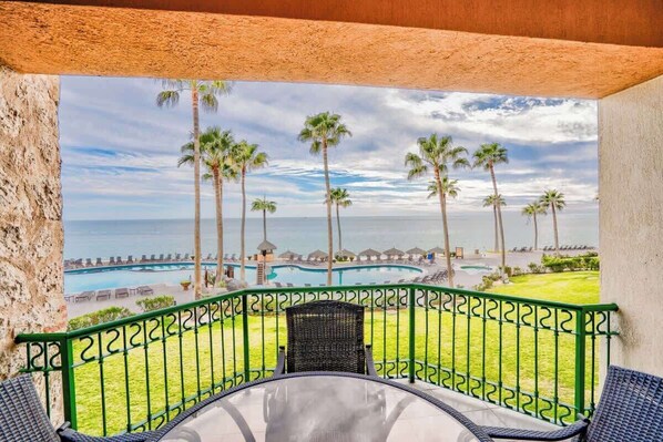 A balcony with a view of a pool and palm trees, a chair, and a railing.