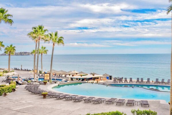 A resort pool area with lounge chairs, palm trees, and a view of the ocean.