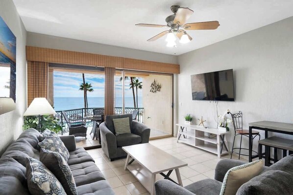 A modern living room with a sofa set, a coffee table, a dining table, and a TV mounted on the wall.