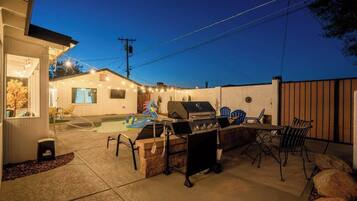 An outdoor patio area with a barbecue grill, seating, and a swimming pool.