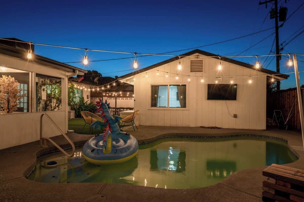 A backyard with a swimming pool, inflatable float, string lights, and a small building.