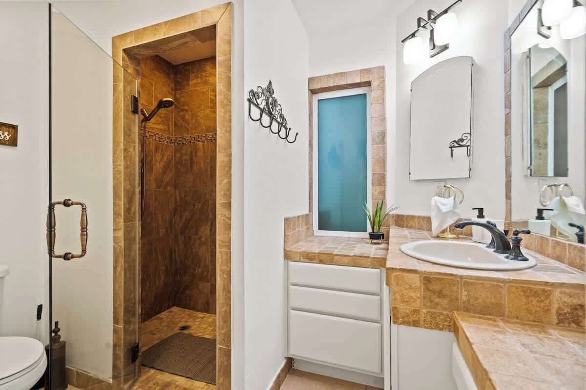 Un baño con ducha envuelta en vidrio, un lavabo blanco sobre encimera color beige y un espejo encima del lavabo.