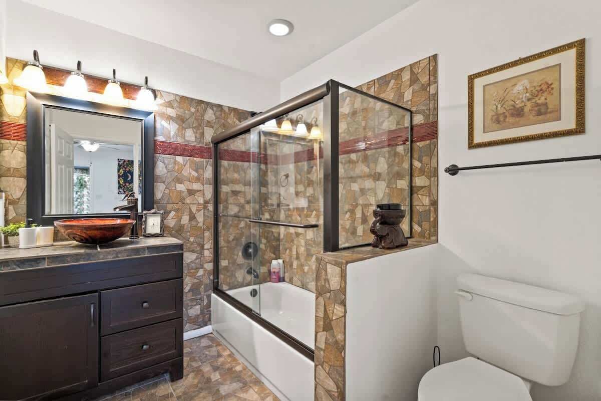 A bathroom with a stone wall, a glass shower enclosure, a white toilet, and a dark wooden vanity.
