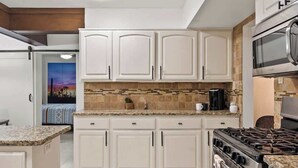 Una cocina con armarios blancos, cocina a gas y microondas.