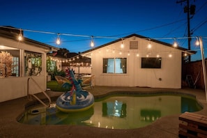 A backyard with a swimming pool, a decorative dragon float, string lights, and a white building. - Oak Scottsdale  · BOHO Scottsdale Oasis Getaway|Pool|ZenRoom (Scottsdale)