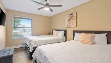 A bedroom with two beds, a ceiling fan, a window with blinds, and a mounted TV.
