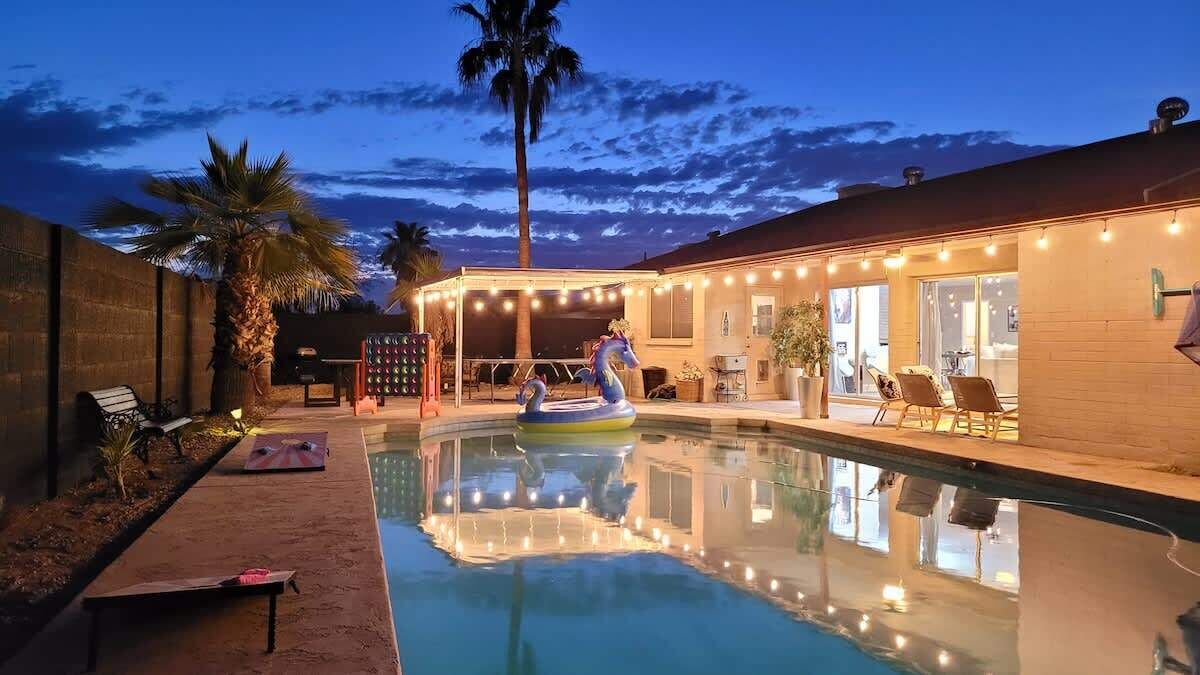 A swimming pool with a lounge area, palm trees, and string lights.
