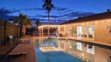 A swimming pool with a lounge area, palm trees, and string lights.