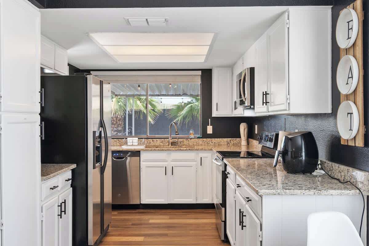 A modern kitchen with white cabinetry, a stainless steel refrigerator, a built-in oven, and a countertop with a coffee maker.