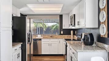 A modern kitchen with white cabinetry, a stainless steel refrigerator, a built-in oven, and a countertop with a coffee maker.