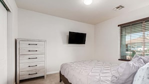 A bedroom with a bed, a dresser, a television, and a window with blinds.