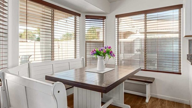 A dining area with a wooden table, white chairs, and a vase with flowers.