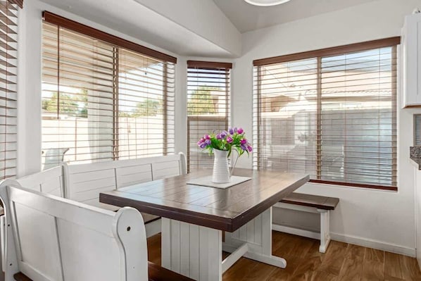 A dining area with a wooden table, white chairs, and a vase with flowers.