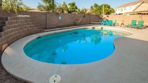 A swimming pool with a curved edge, surrounded by a brick wall and a concrete deck.