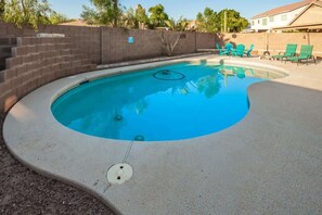A swimming pool with a curved edge, surrounded by a brick wall and a concrete deck.