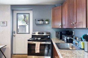 A kitchen with a stainless steel stove, a microwave, and a sink. There is a door with a 'No Parking' sign, a shelf with plants, and wooden cabinets. - Downtown Renovated Apt w/ Free Parking & BBQ (Phoenix)