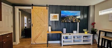 A room with a wooden floor, a sliding barn door, a white console table, a framed picture, and a window with blinds.