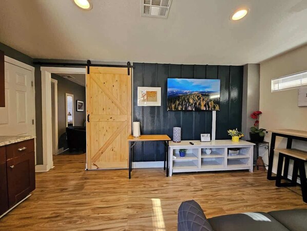 A room with a wooden floor, a sliding barn door, a white console table, a framed picture, and a window with blinds.