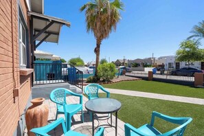 Eine Terrasse mit Gartenmöbeln, einer Palme und einem eingezäunten Bereich mit Autos.