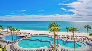 Een resort met een groot, kronkelend zwembad, omringd door palmbomen en strandstoelen, met uitzicht op een heldere blauwe zee.