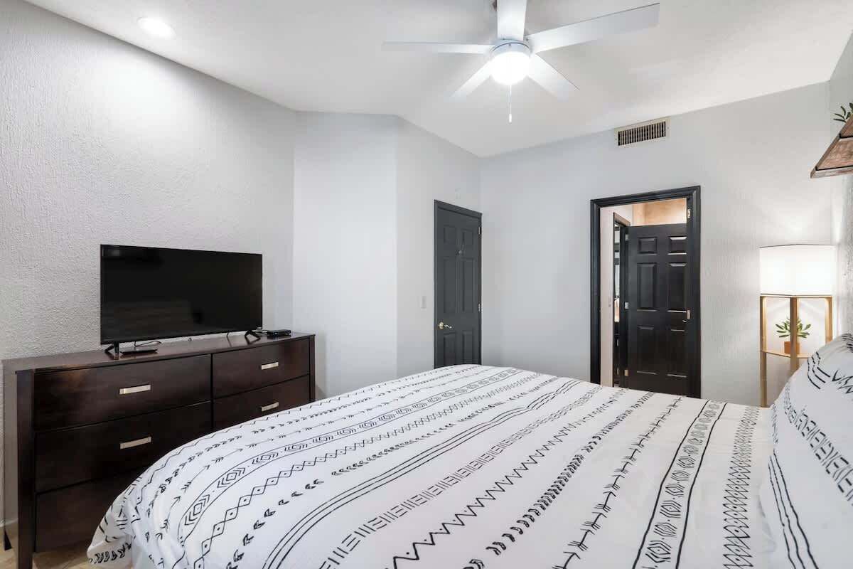 A bedroom with a bed, a dresser, a television, a ceiling fan, and a door.