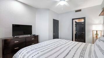 A bedroom with a bed, a dresser, a television, a ceiling fan, and a door.