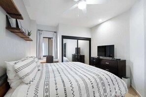 A bedroom with a bed, a TV, a dresser, and a mirror.