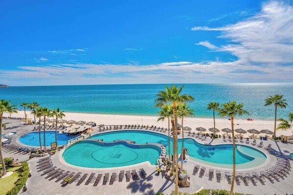Un resort con una amplia zona de piscina, palmeras y vistas a la playa.