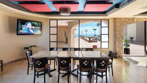 Un comedor con una mesa grande y sillas, un televisor montado en la pared y vistas a un patio exterior.