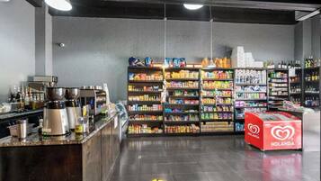 Ein Supermarktinneres mit Regalen voller verschiedener Produkte, einer Kaffeemaschine und einem roten HOLANDA-Kühlschrank.