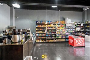 L’intérieur d’une épicerie, avec des étagères remplies de divers produits, un appareil à café et un réfrigérateur rouge de la marque HOLANDA.