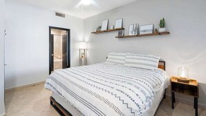 Een slaapkamer met een bed, een plafondventilator, een wandplank met foto’s en een bedlampje.