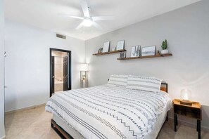 Une chambre à coucher comprenant un lit, un ventilateur de plafond, une étagère murale avec des photos et une lampe de chevet.