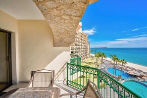 Un balcon avec vue sur une plage et une piscine, comprenant une chaise et une table.