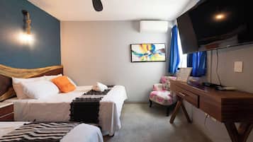 A hotel room with two beds, a desk, a chair, a TV, and a ceiling fan.