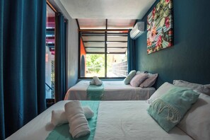 Ein Zimmer mit zwei Betten, einem Fenster mit Vorhängen, einer Wandklimaanlage und einem farbenfrohen Gemälde.