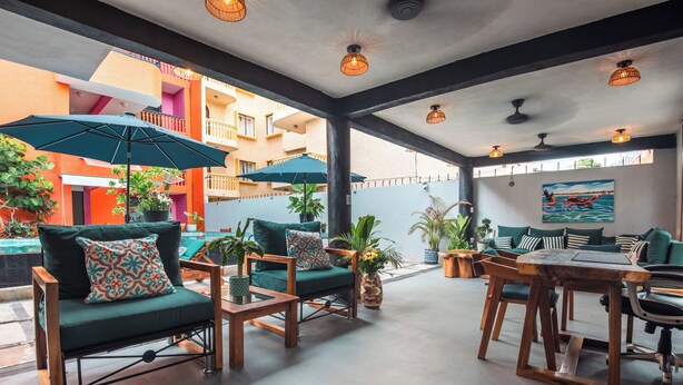 An outdoor seating area with wooden furniture and umbrellas, surrounded by potted plants and a view of a building with balconies. - Zihua Mia Hotel Boutique 3 (Zihuatanejo)