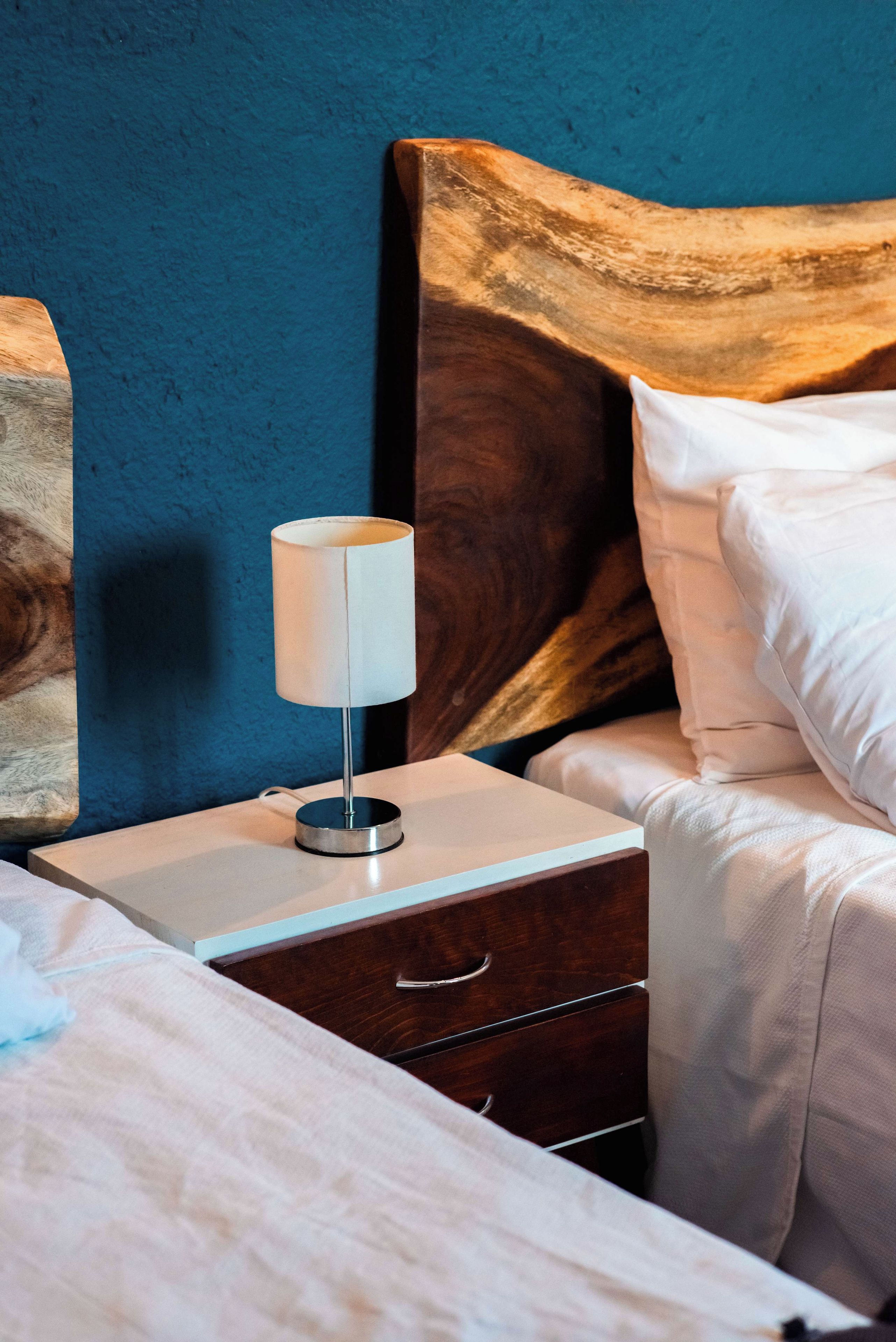 Un lit bien fait, avec du linge de lit blanc, une table de chevet avec une lampe et une tête de lit en bois.