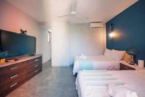 Una camera da letto con una TV, due letti, una ventola a soffitto e un comodino con una lampada.