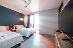 Une chambre avec deux lits, un ventilateur de plafond, une table de chevet, une commode et une fenêtre avec des rideaux.