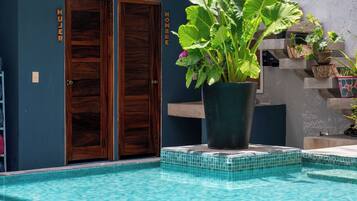 A pool area with a wooden door labeled 'Mujer' and 'Hombre,' a potted plant, and a tiled edge.