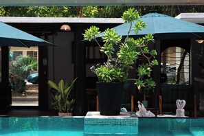 A pool area with a tiled edge, potted plants, and umbrellas.
