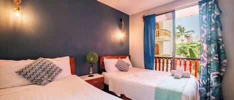 A hotel room with two beds, a nightstand with a lamp, a window with curtains, and a balcony with a railing.