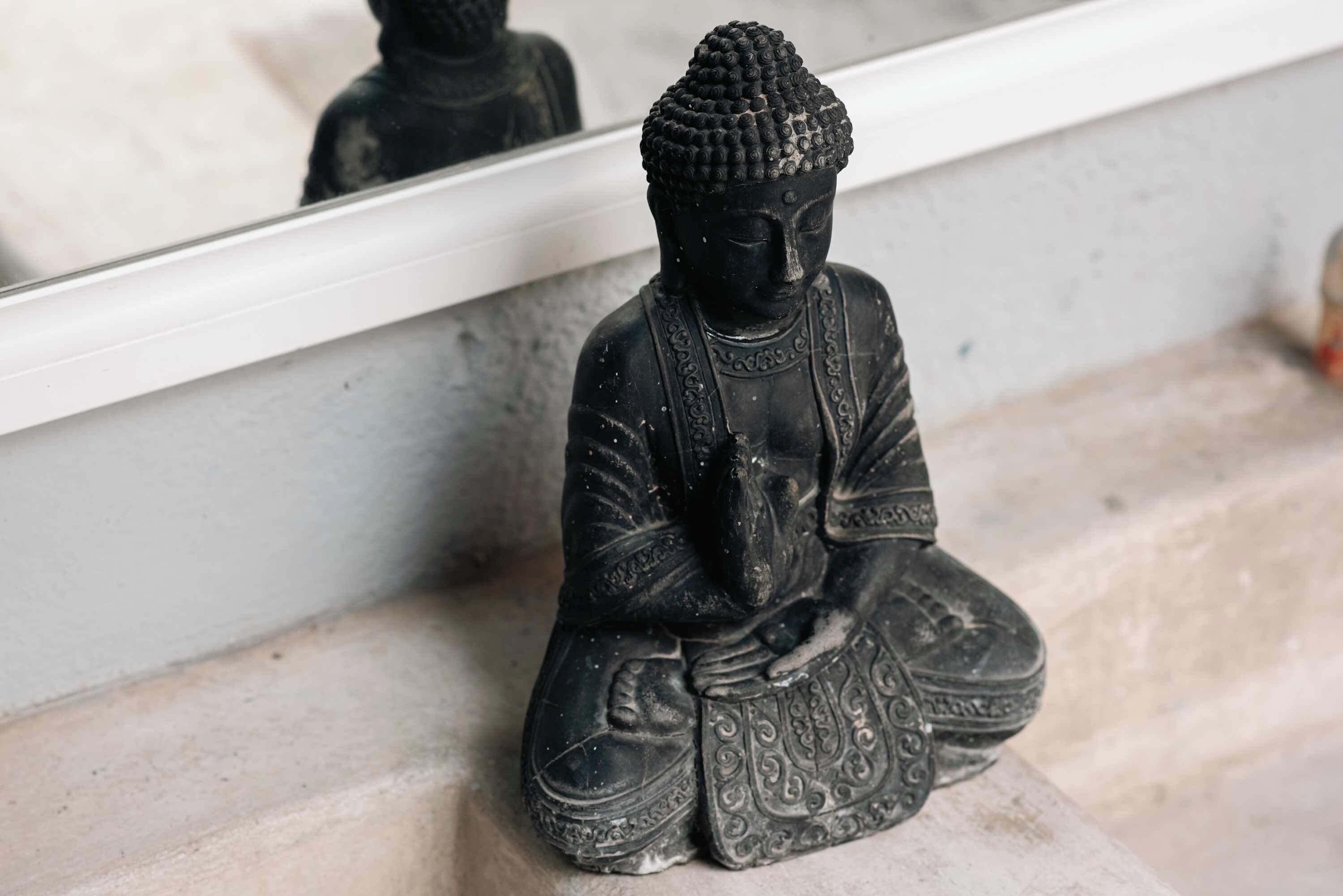 Une statue représentant une figure assise, ornée de sculptures complexes, et placée sur un piédestal en pierre.