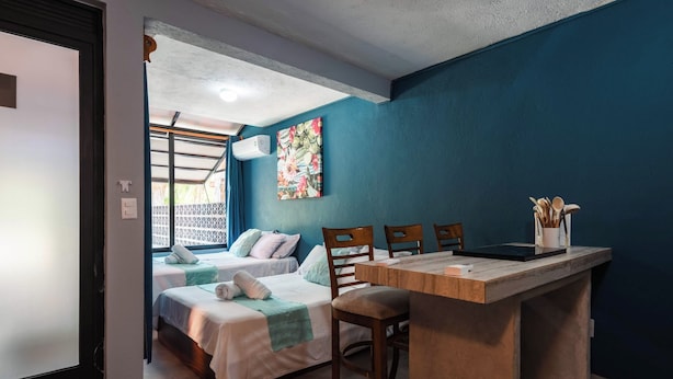 A room with two beds, a wooden desk, chairs, a painting, and a window with a view. - Zihua Mia Hotel Boutique 5 (Zihuatanejo)