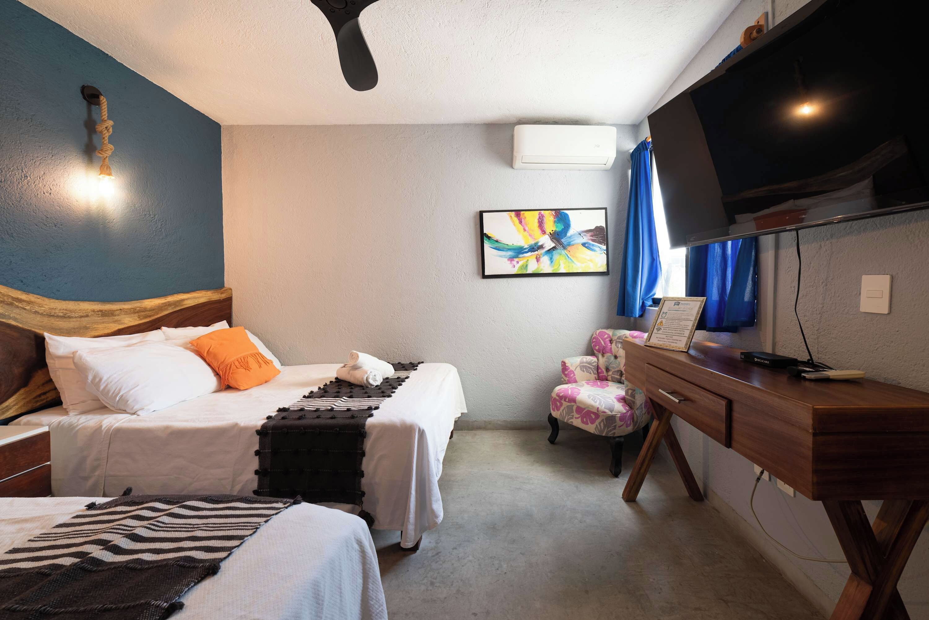 A hotel room with two beds, a desk, a chair, a TV, and a ceiling fan.