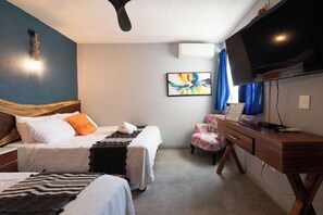 A hotel room with two beds, a desk, a chair, a TV, and a ceiling fan.